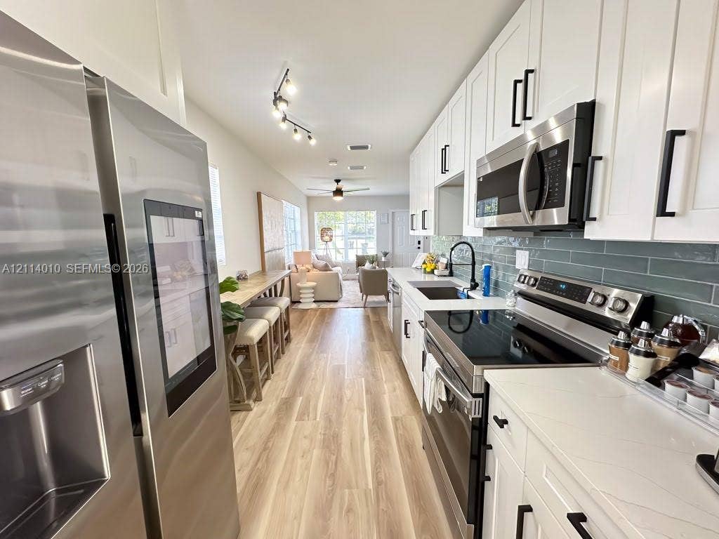 1161-1163 SW 30th Street, Fort Lauderdale, FL 33315 Kitchen featuring white shaker-style cabinetry, quartz countertops, stainless steel appliances, a green subway tile backsplash, and wood-finish flooring