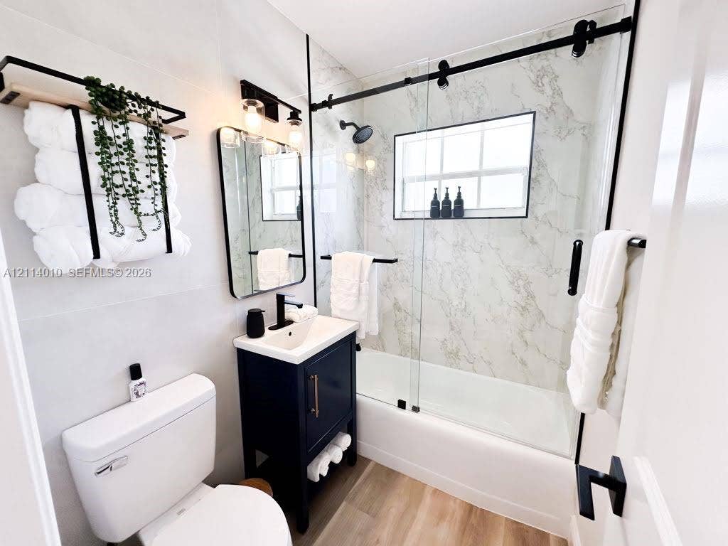 1161-1163 SW 30th Street, Fort Lauderdale, FL 33315 Bathroom featuring a vanity with a rectangular sink, stone-patterned shower surround, glass sliding shower door with matte black hardware, and wood-finish flooring