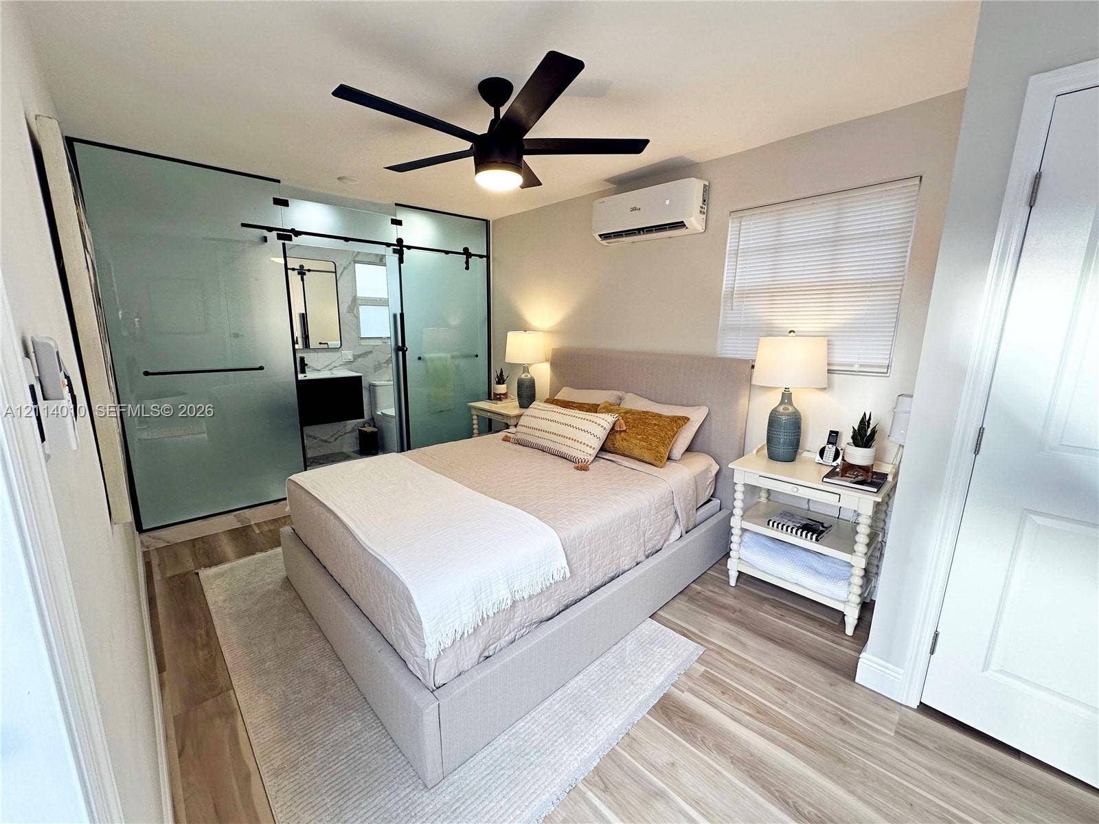 1161-1163 SW 30th Street, Fort Lauderdale, FL 33315 Frosted glass sliding barn doors, wood-finish flooring, ceiling fan with integrated lighting, and wall-mounted ductless air conditioning unit