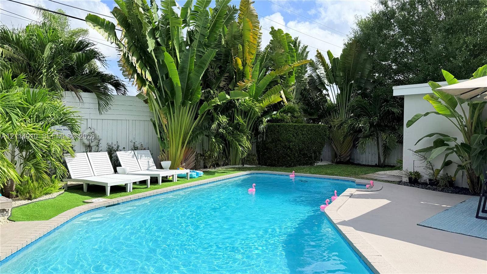 1161-1163 SW 30th Street, Fort Lauderdale, FL 33315 In-ground swimming pool featuring a concrete deck, enclosed by perimeter fencing, mature tropical landscaping, and artificial turf surfacing