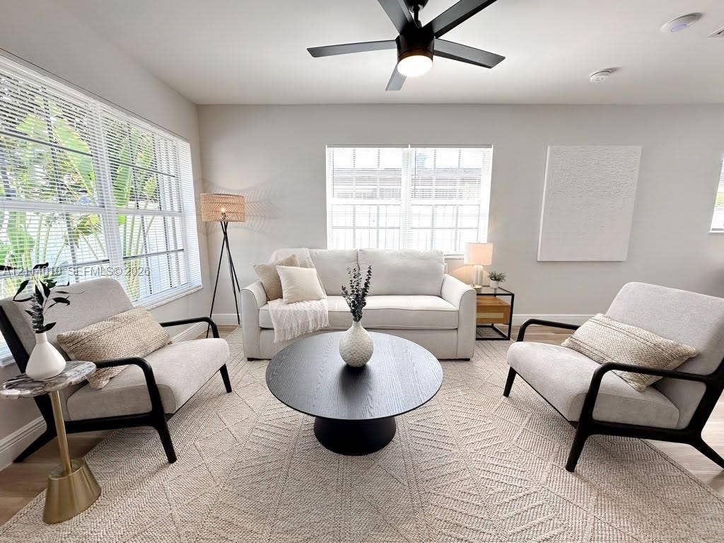 1161-1163 SW 30th Street, Fort Lauderdale, FL 33315 Living area featuring light-toned walls, wood-finish flooring, dual-pane windows with horizontal blinds, and a central ceiling fan with integrated lighting