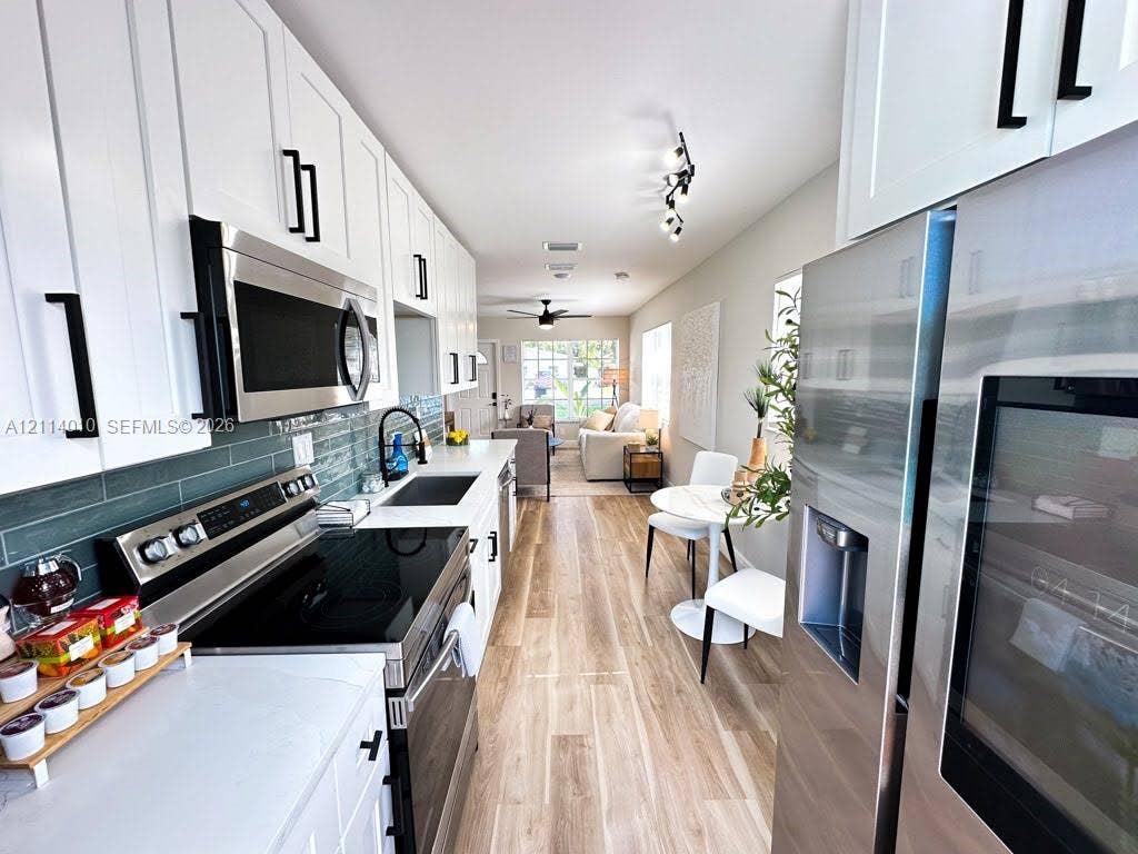 1161-1163 SW 30th Street, Fort Lauderdale, FL 33315 Kitchen featuring white Shaker-style cabinetry, stainless steel appliances, wood-finish flooring, quartz countertops, and a blue subway tile backsplash