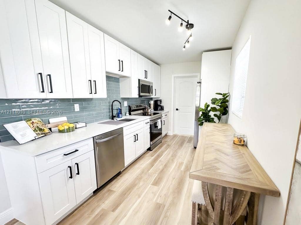 1161-1163 SW 30th Street, Fort Lauderdale, FL 33315 Kitchen featuring white shaker-style cabinetry, light-toned countertop, blue glass tile backsplash, stainless steel appliances, and wood-finish flooring