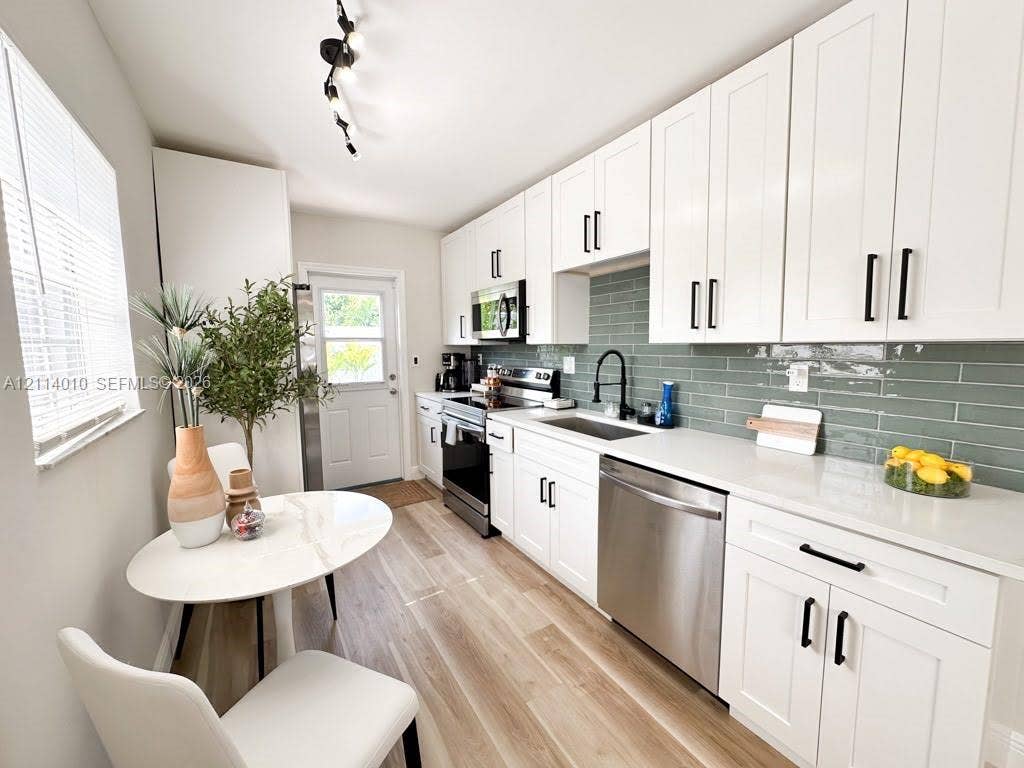 1161-1163 SW 30th Street, Fort Lauderdale, FL 33315 Kitchen featuring white shaker-style cabinetry, solid-surface countertops, subway-style tile backsplash, stainless steel appliances, and wood-finish flooring