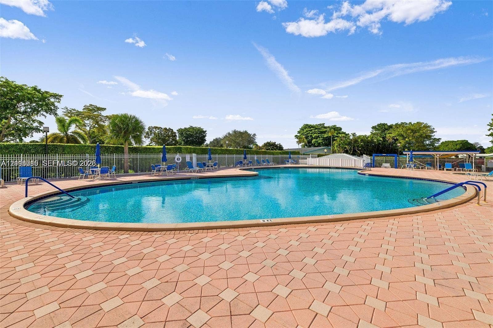Swimming pool with curved edge, integrated steps, metal handrails, and a surrounding paver deck