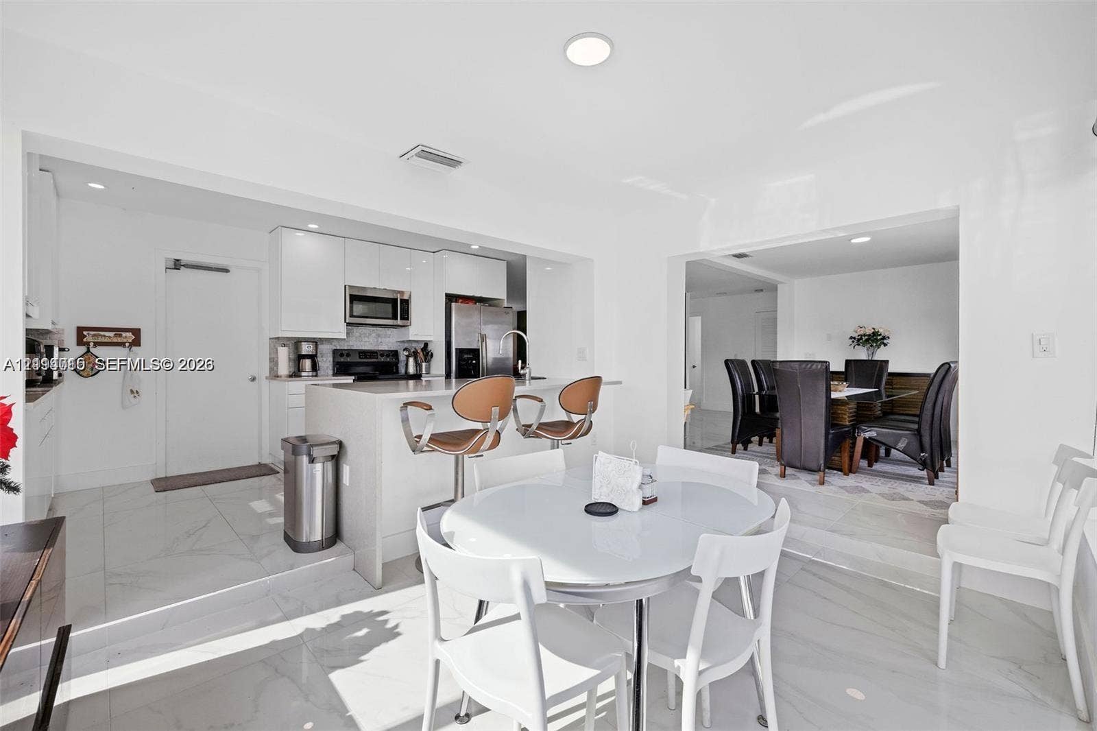 Kitchen featuring white flat-panel cabinetry, quartz countertops, a waterfall-edge breakfast bar, stainless steel appliances, and large-format porcelain tile flooring