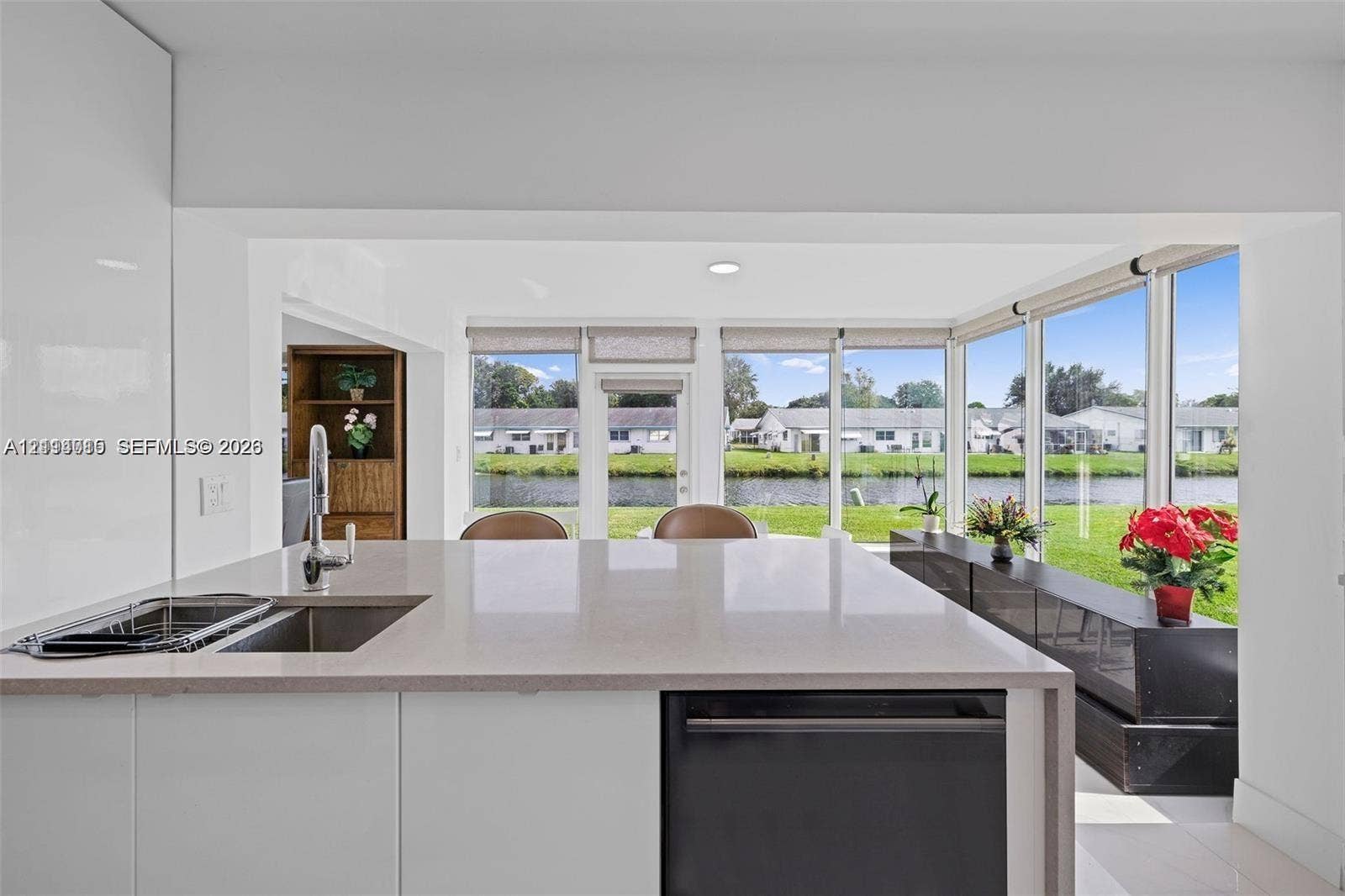 Kitchen featuring a white island with a solid surface countertop, an undermount stainless steel sink, and a built-in dishwasher