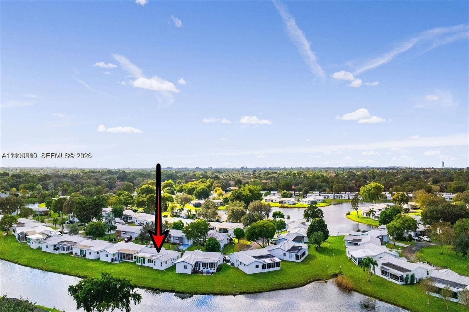 Aerial perspective of a single-story residence featuring a white exterior, a low-pitch roof, and direct water frontage along a perimeter canal