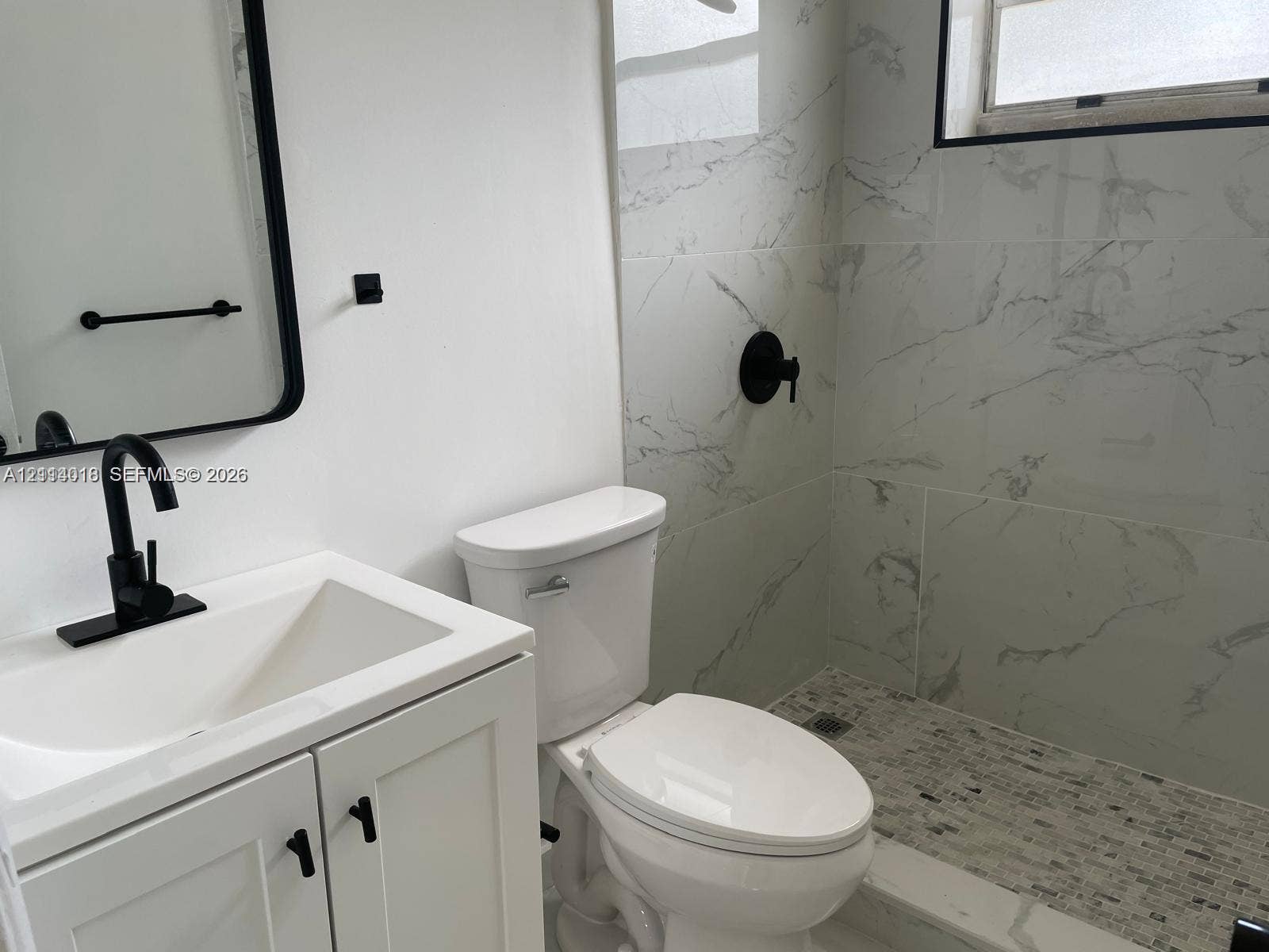6029 Polk Street, #1B, Hollywood, Hollywood, FL 33024 Bathroom featuring a white vanity cabinet, rectangular vessel sink with a matte black faucet, framed vanity mirror, walk-in shower with large-format wall tiling, and mosaic-tiled shower flooring