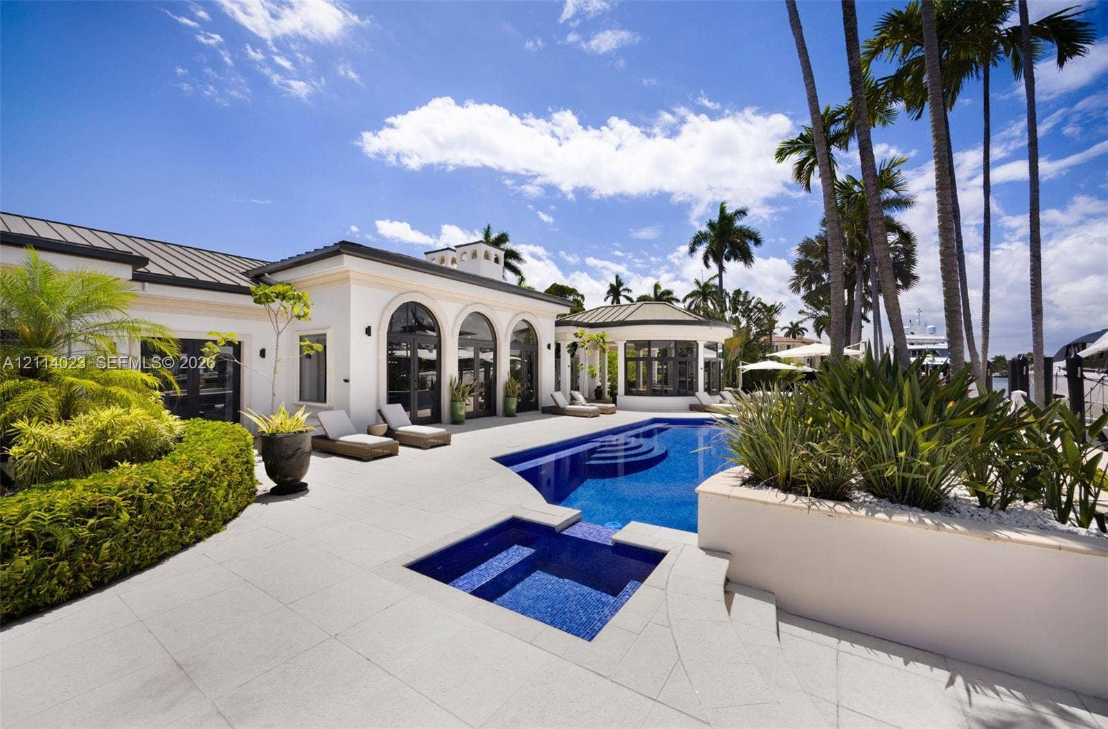 Outdoor living area featuring a tile-surround pool and spa, arched architectural openings, manicured landscaping, and a metal roof