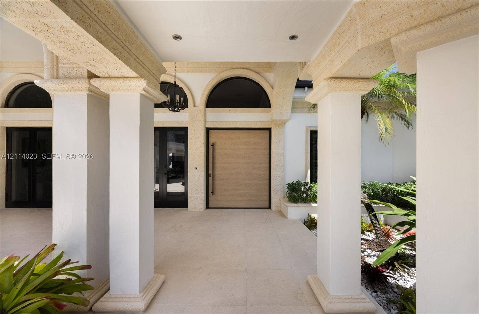 Covered entryway featuring structural stone columns, arched overhead detailing, a central oversized wood-finish door, and integrated recessed lighting