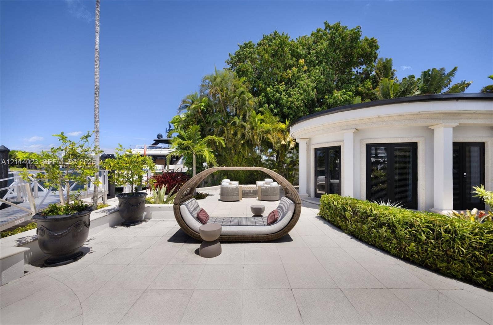 Waterfront terrace featuring large-format tile flooring, a curved architectural exterior wall with columns, French door access, and professional landscaping