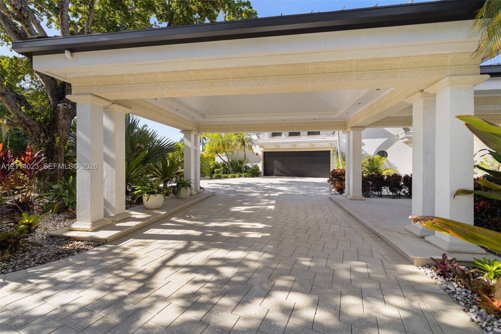 Covered porte-cochere featuring structural columns, recessed lighting, and a paved stone driveway leading to a multi-car garage
