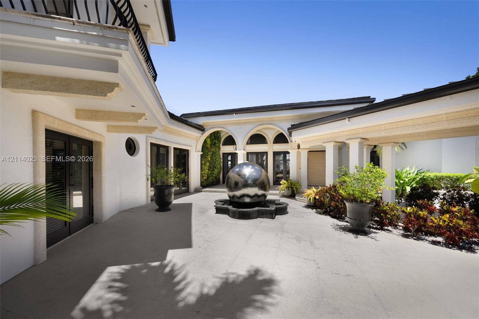 Courtyard featuring stone-tiled flooring, arched colonnades, a central metallic sphere water feature, and exterior masonry detailing