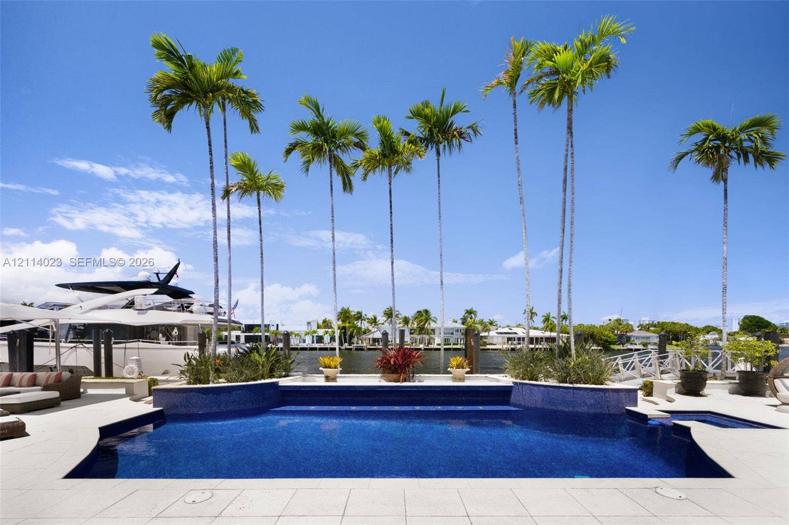 Waterfront pool featuring a mosaic-tile finish, elevated spa, stone-paver decking, and manicured palm tree landscaping