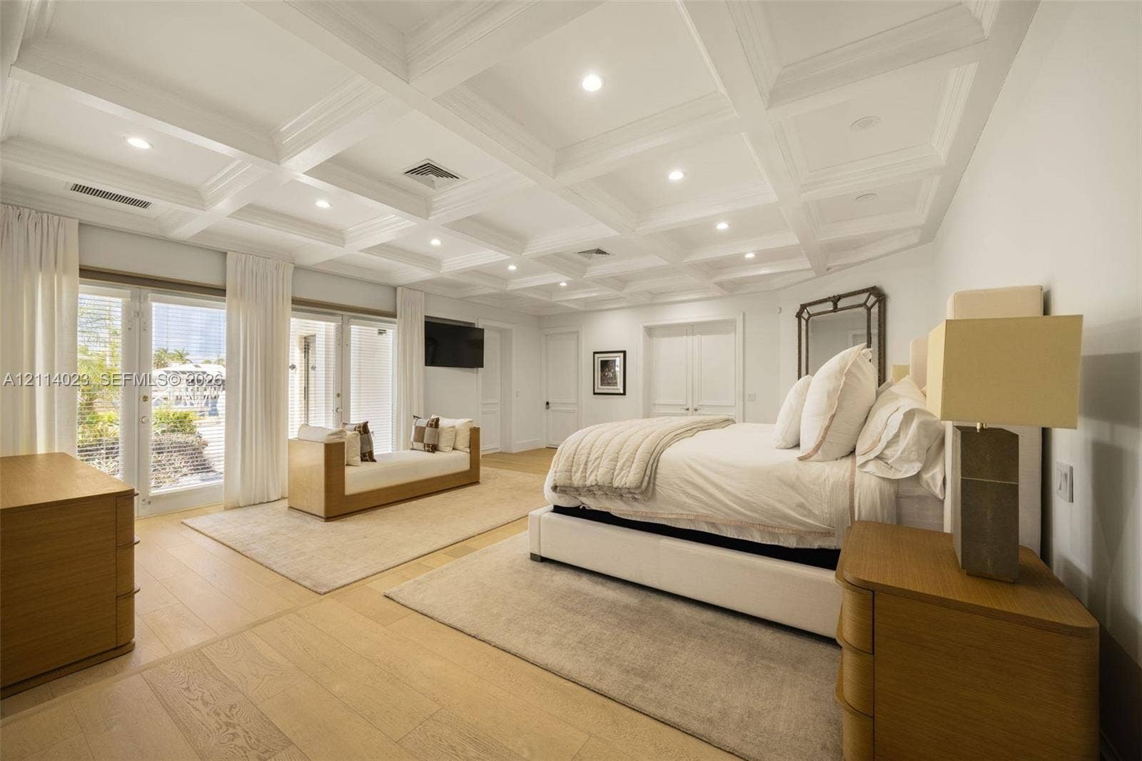 Coffered ceiling with recessed lighting, wood-finish flooring, and double glass-paneled doors providing exterior access