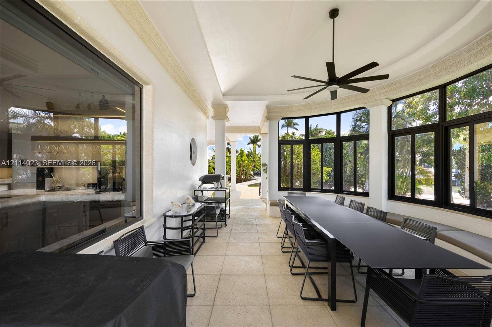 Covered outdoor loggia featuring light-toned tile flooring, recessed ceiling lighting, a modern ceiling fan, and black-framed windows with built-in bench seating