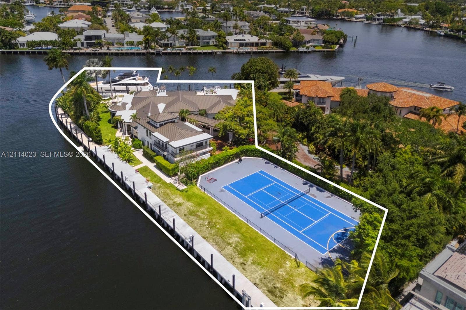 Waterfront estate featuring a private tennis court, expansive bulkhead dockage, multi-level residence with a multi-hipped roof, and mature perimeter landscaping