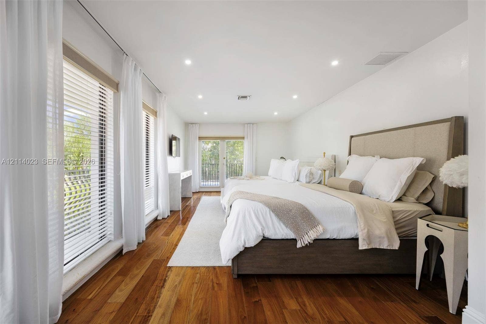 Wood-finish flooring, recessed lighting, multiple floor-to-ceiling windows, and glass-paneled double doors opening to an exterior balcony