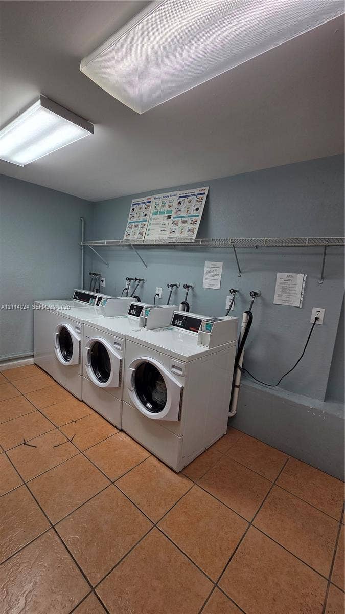 505 S Pine Island Road, #B205, Plantation, FL 33324 Laundry area featuring ceramic tile flooring, three white front-load washers, and a wall-mounted wire storage shelf