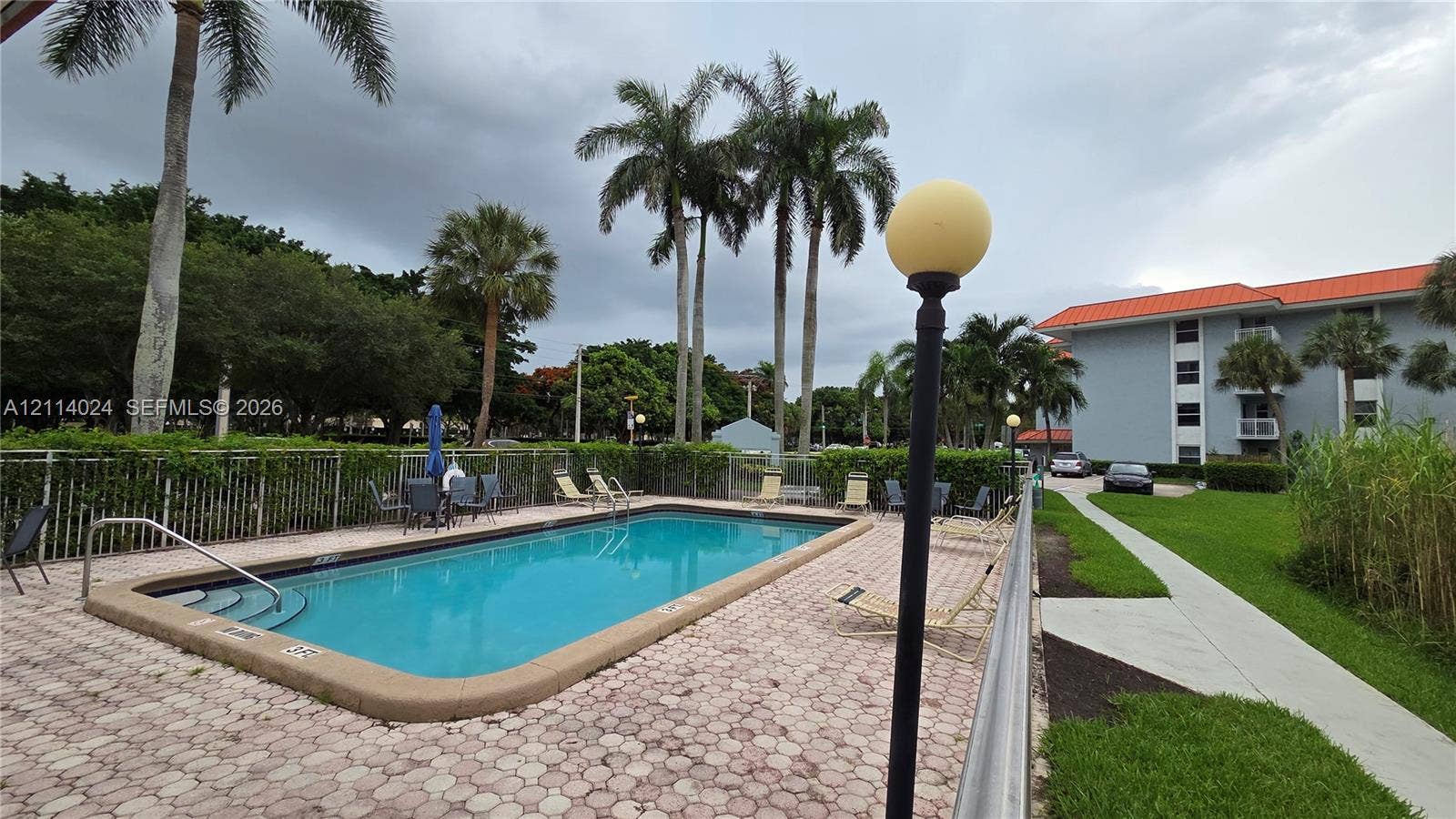 505 S Pine Island Road, #B205, Plantation, FL 33324 Swimming pool featuring a concrete paver deck, metal perimeter fencing, and mature palm trees