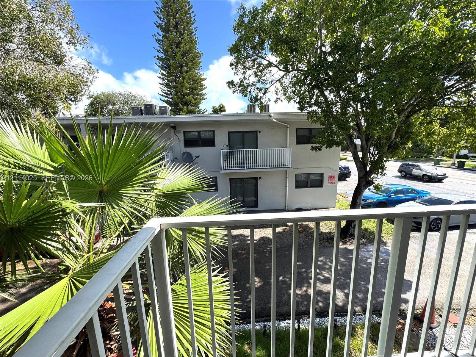 1505 NE 135th Street, #10, North Miami, North Miami, FL 33161 Private balcony with vertical metal railing, exterior building facade, and mature landscaping