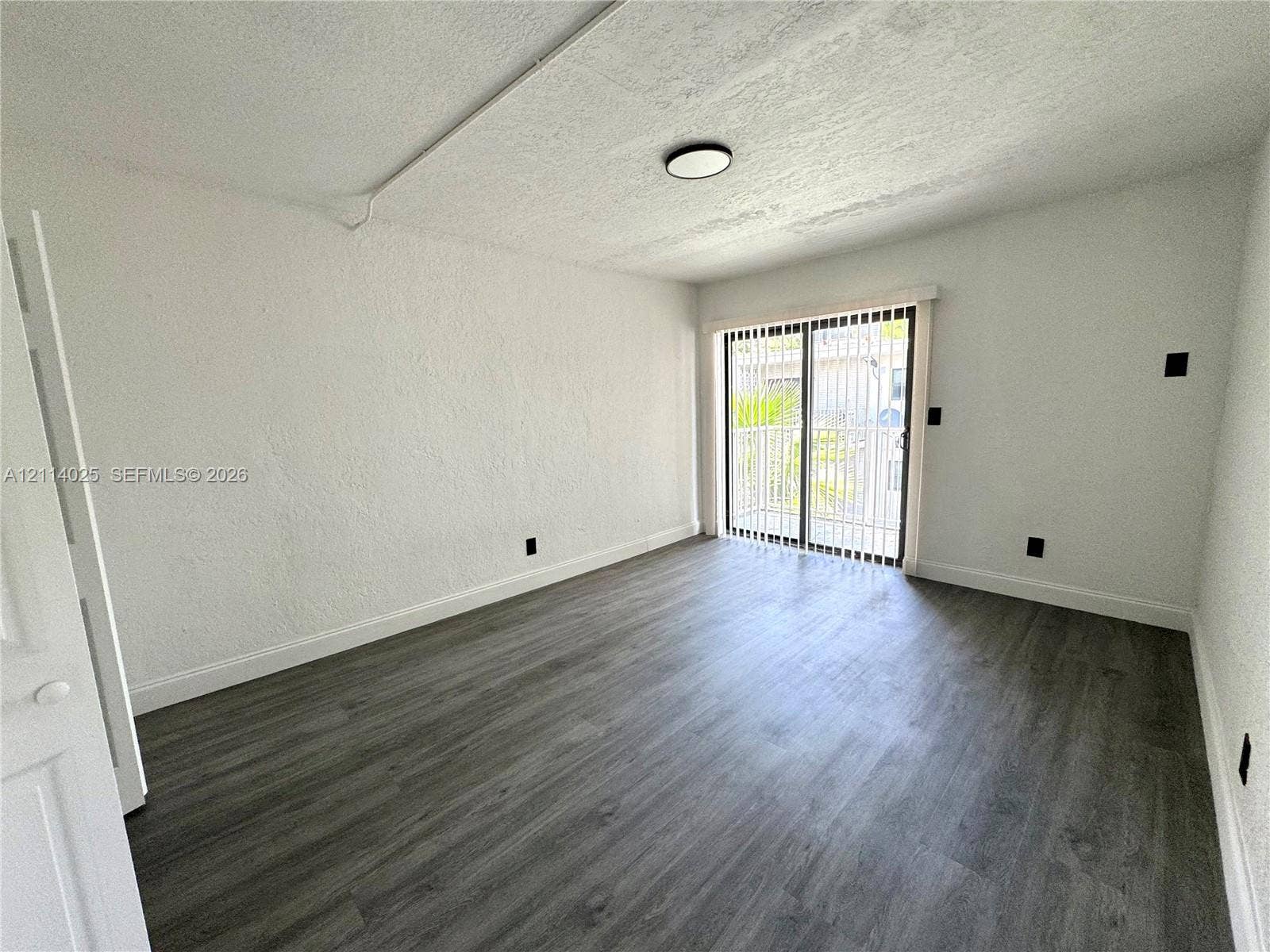 1505 NE 135th Street, #10, North Miami, North Miami, FL 33161 Room featuring wood-finish flooring, textured wall surfaces, and a sliding glass door with vertical blinds