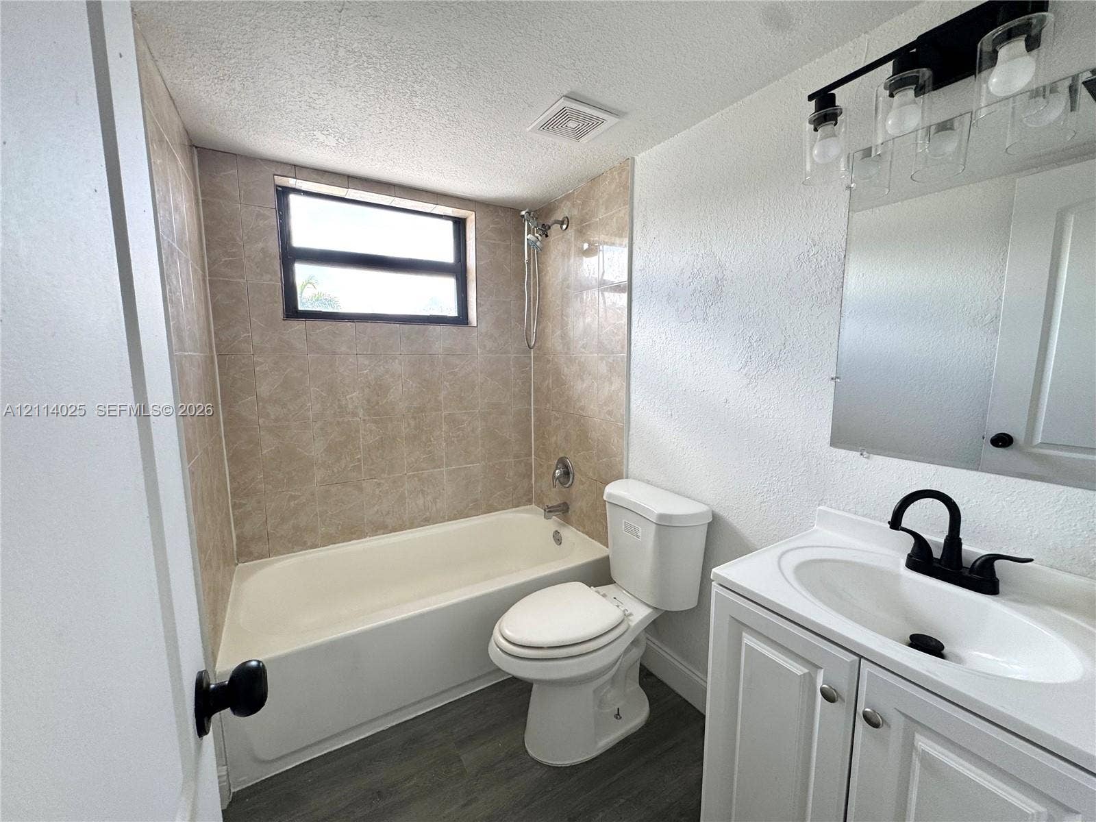 1505 NE 135th Street, #10, North Miami, North Miami, FL 33161 Bathroom featuring a white vanity cabinet with a integrated sink, matte black faucet, and contemporary light fixture, complemented by wood-finish flooring and a tiled shower surround
