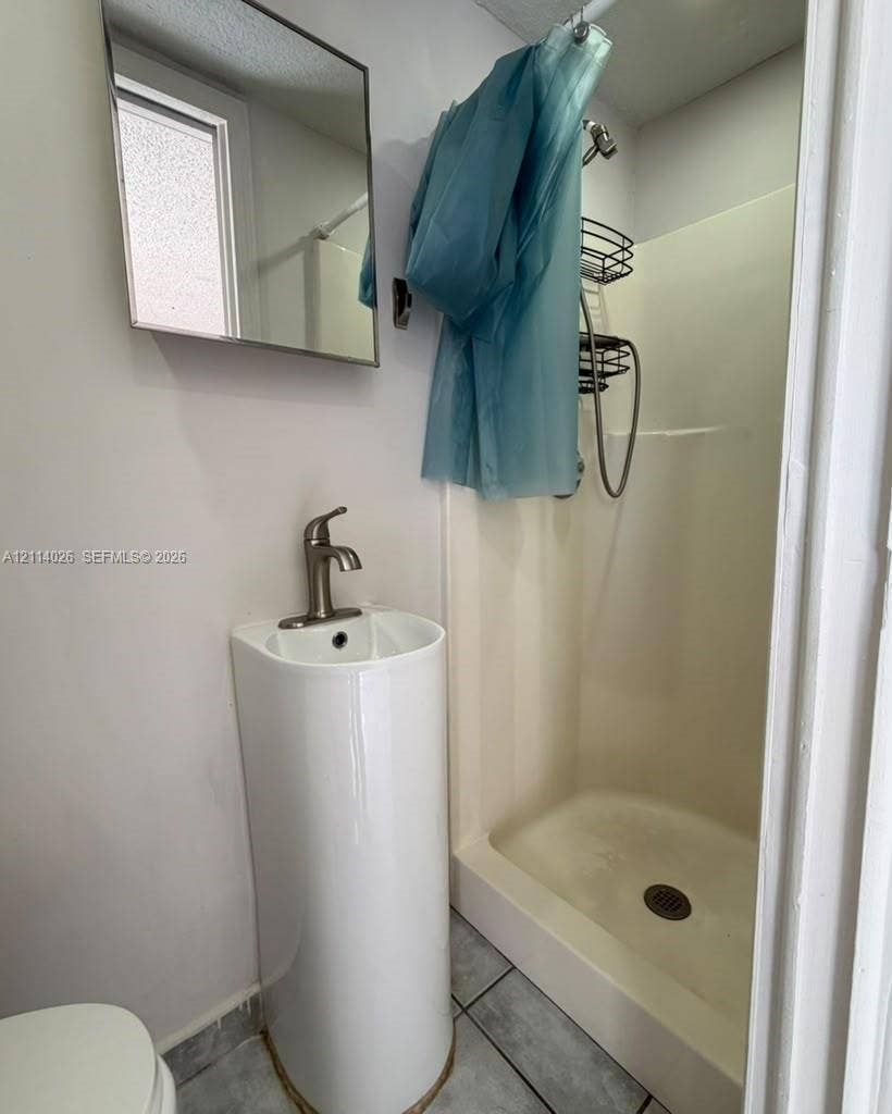 11511 SW 180th Street, #Studio, Miami, Miami, FL 33157 Wall-mounted rectangular mirror, pedestal sink with a single-handle brushed nickel faucet, and a prefabricated shower stall