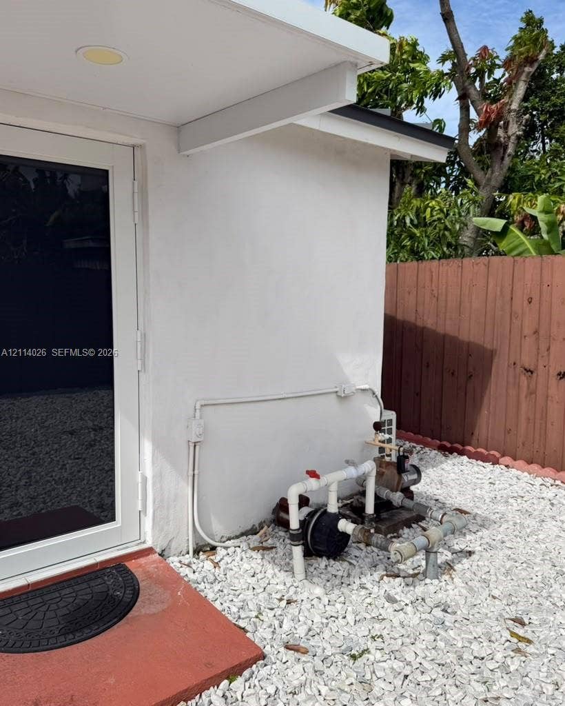 11511 SW 180th Street, #Studio, Miami, Miami, FL 33157 Exterior of the structure featuring white smooth-finish siding, a full-lite glass door, and a white gravel ground cover enclosed by a vertical wood-plank fence