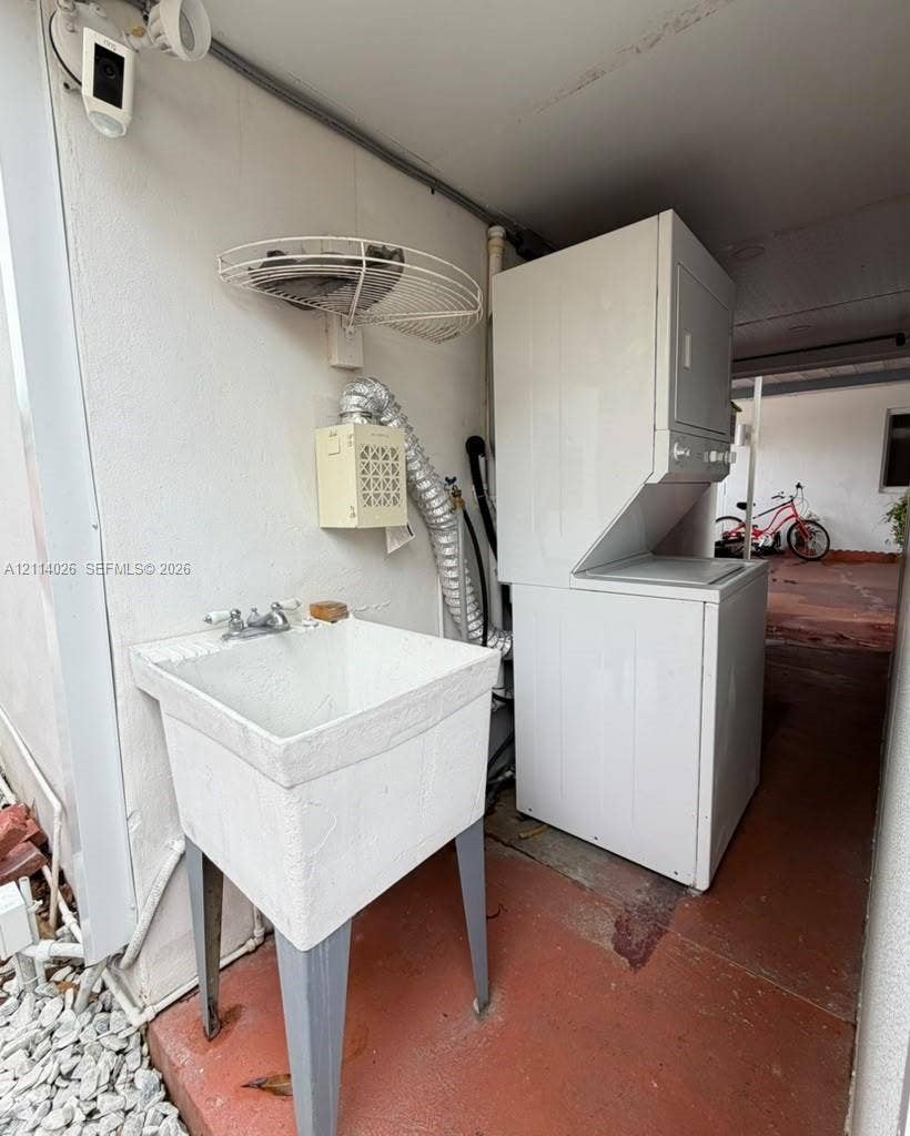 11511 SW 180th Street, #Studio, Miami, Miami, FL 33157 Utility area featuring a floor-mounted basin with dual-handle faucet, stackable laundry unit, wall-mounted wire shelf, and security camera