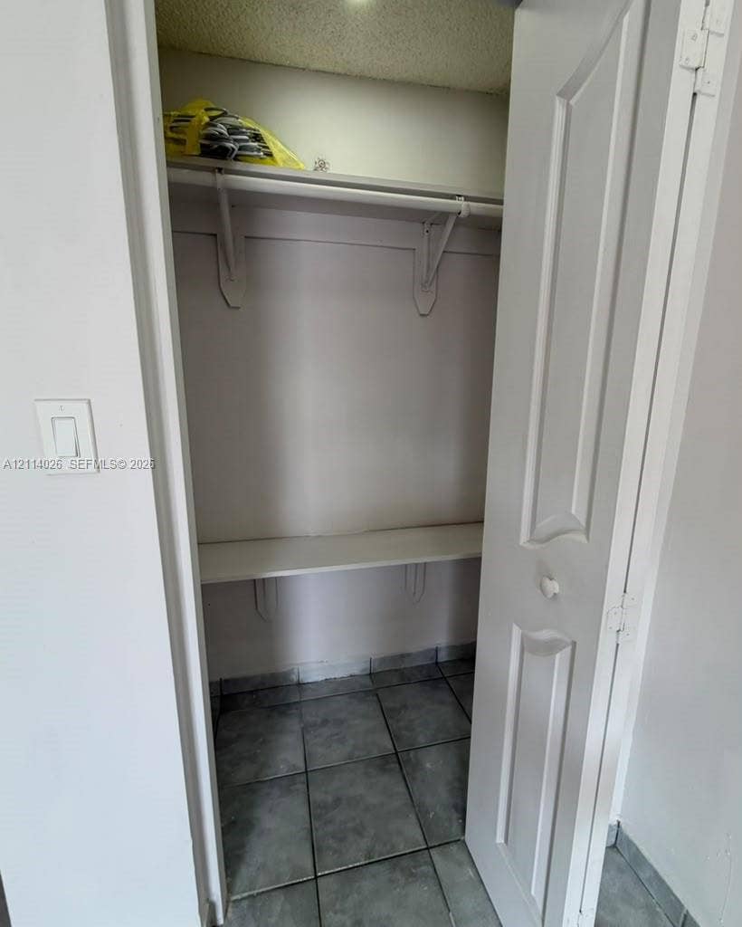 11511 SW 180th Street, #Studio, Miami, Miami, FL 33157 Storage closet featuring tile flooring, two-tiered built-in shelving, and a paneled door