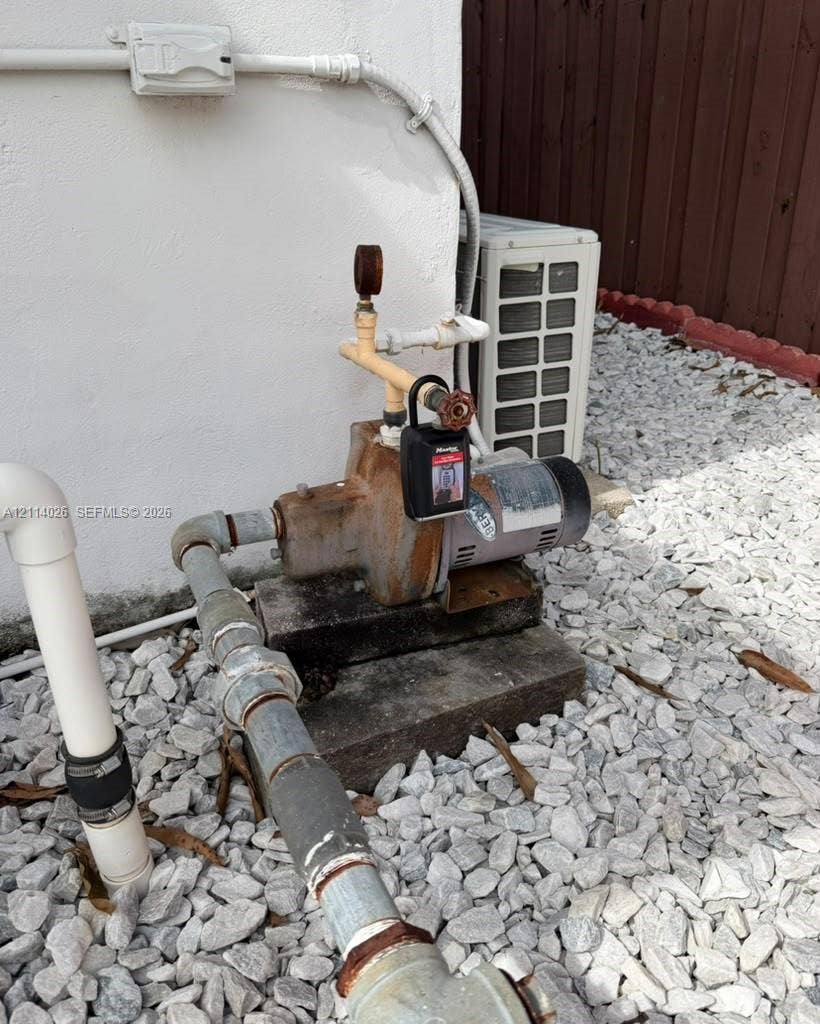 11511 SW 180th Street, #Studio, Miami, Miami, FL 33157 Exterior utility area featuring a water pump system, HVAC condenser unit, and crushed stone ground cover