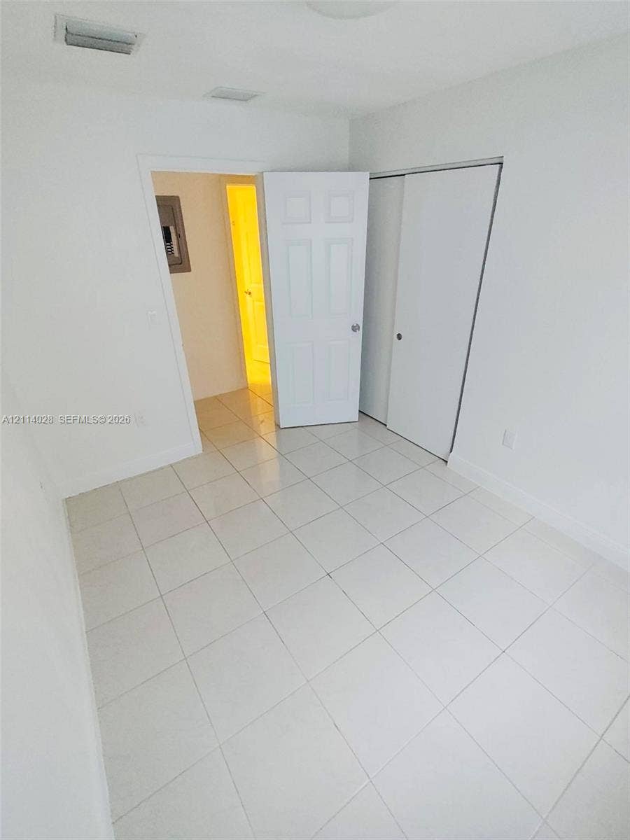 Interior space featuring neutral wall paint, white tile flooring, a six-panel swing door, and a sliding-door closet