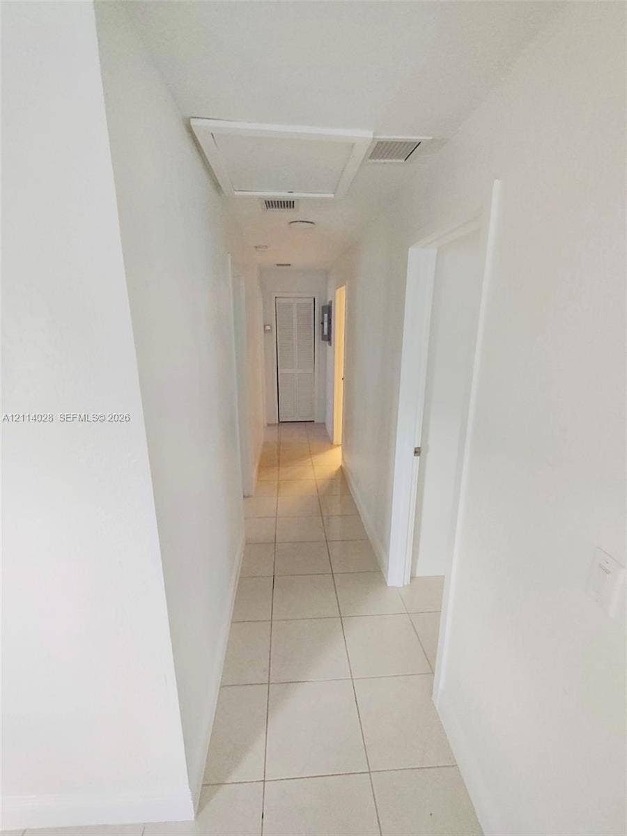 Hallway featuring large-format ceramic tile flooring, neutral wall finishes, recessed lighting, and louvered closet doors
