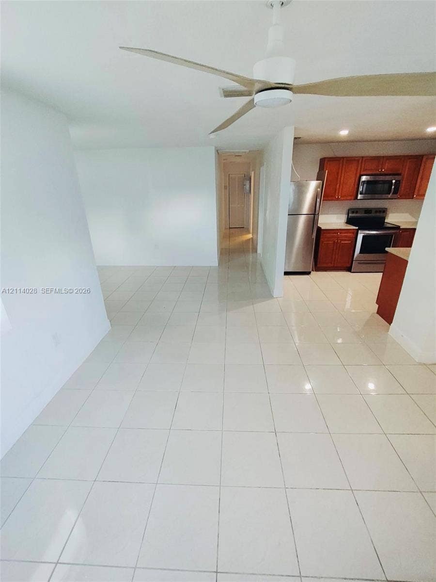 Neutral tile flooring, kitchen featuring wood cabinetry, stainless steel appliances, and ceiling fan with integrated lighting