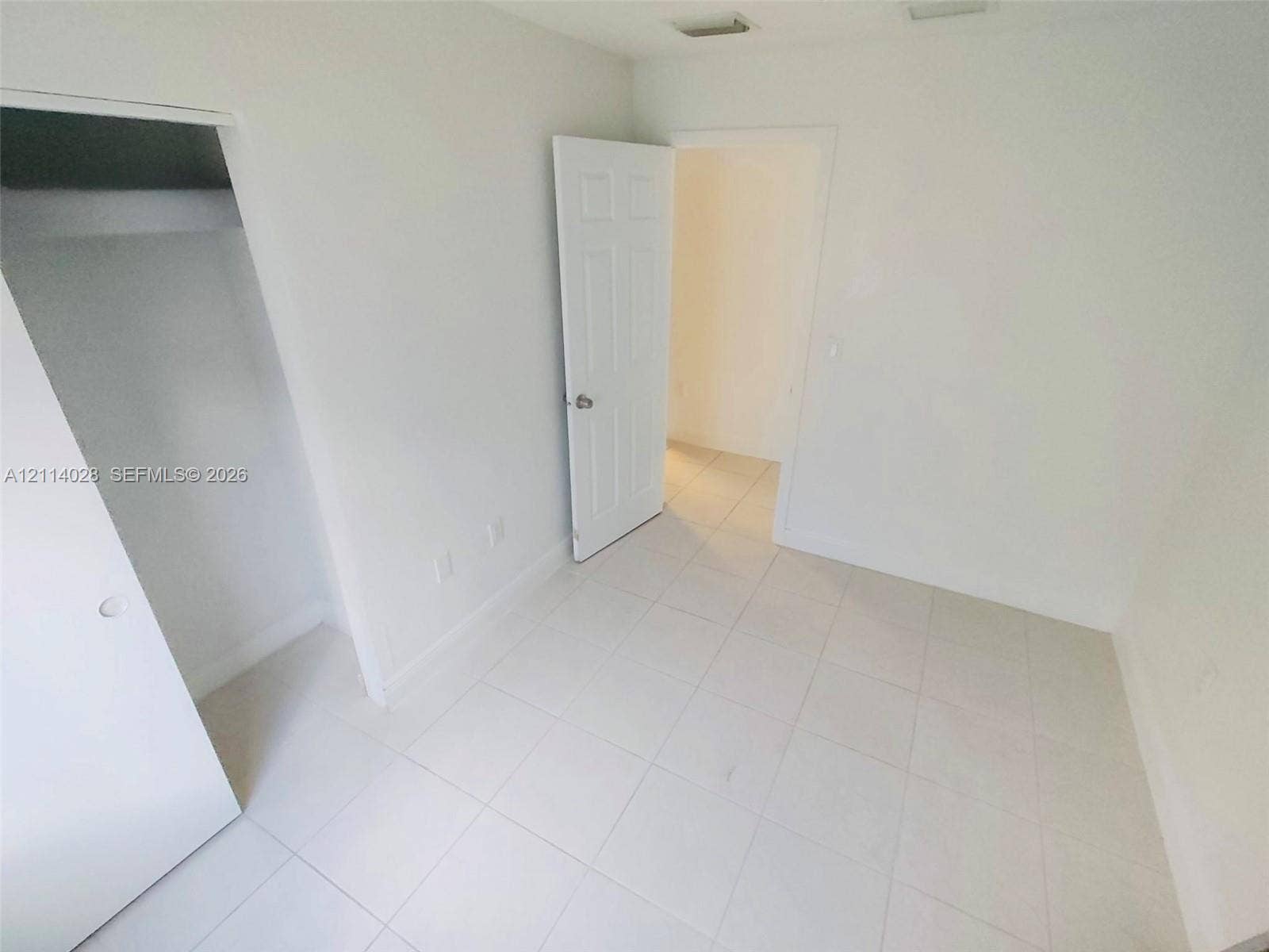 Interior room featuring neutral ceramic tile flooring, six-panel doors, and a built-in closet with a shelf