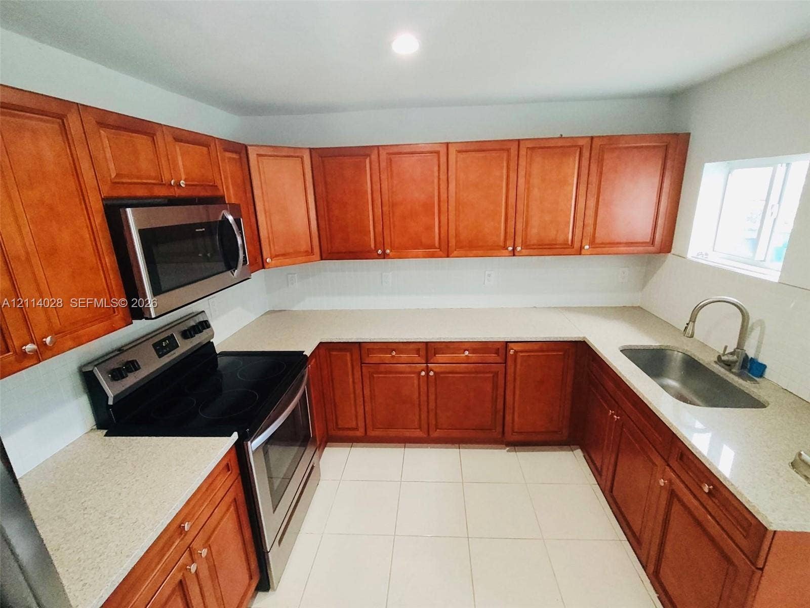 Kitchen featuring wood cabinetry, stone-composite countertops, stainless steel appliances, ceramic tile flooring, and a single-basin undermount sink