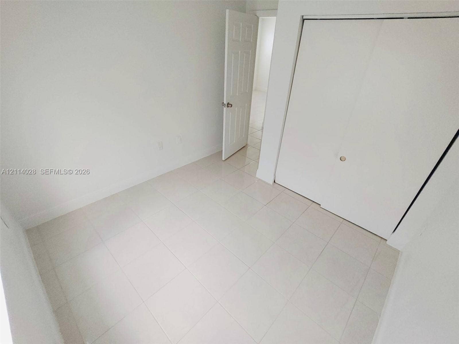 Interior space featuring white-toned tile flooring, neutral walls, a six-panel door, and a built-in closet with sliding doors