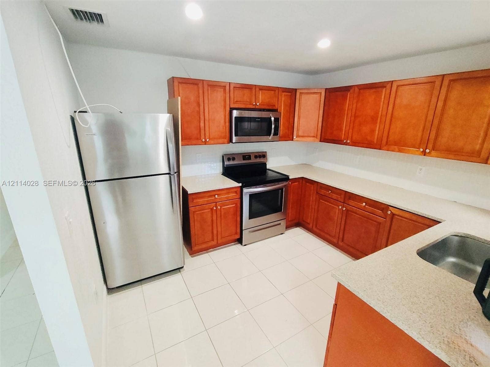 Kitchen featuring wooden cabinetry, solid surface countertops, stainless steel refrigerator, stainless steel microwave, and stainless steel electric range