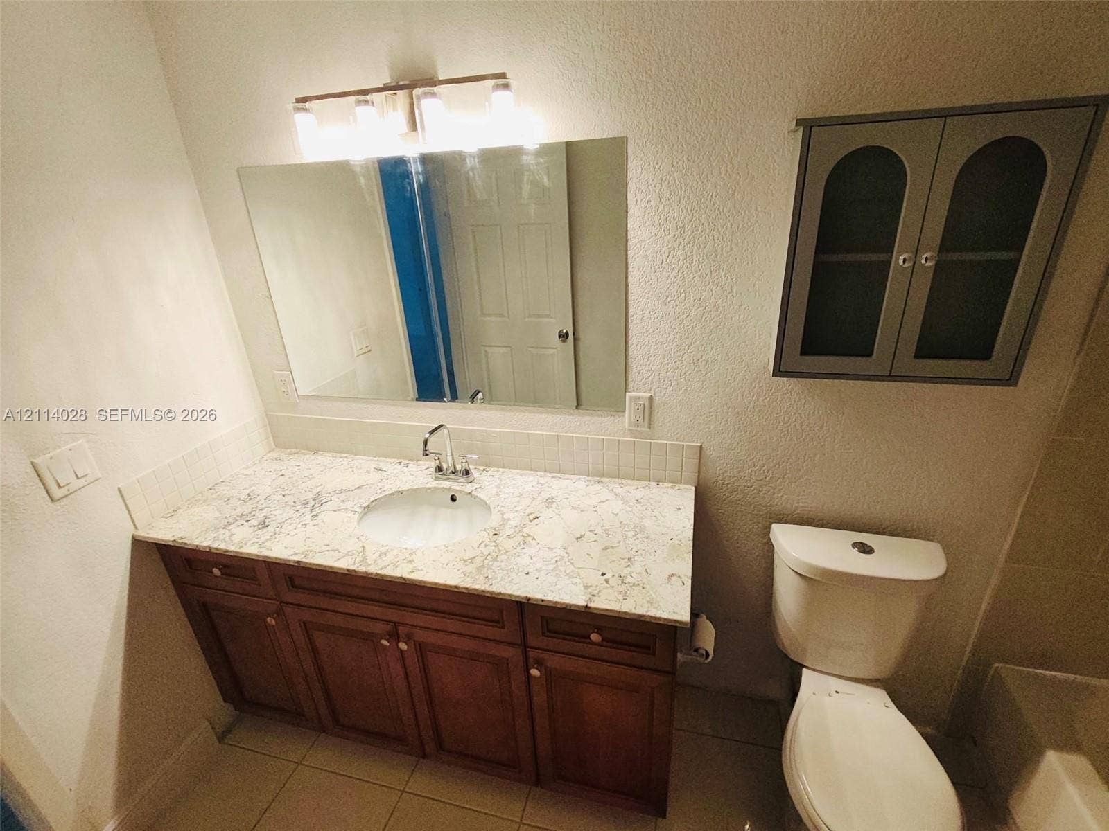 Bathroom vanity featuring a stone-look countertop, integrated ceramic sink, wood-finish cabinetry, a wall-mounted medicine cabinet, and a multi-bulb light fixture
