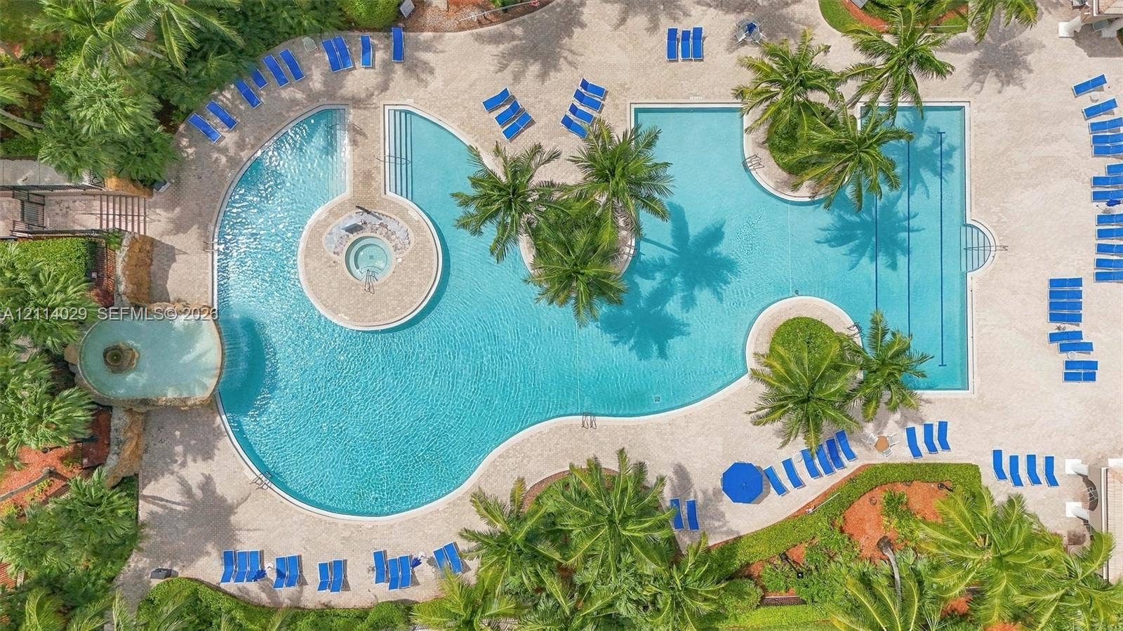 5257 SW 158th Avenue, Miramar, FL 33027 Expansive swimming pool featuring an integrated spa, a stone-accented water feature, palm landscaping, and stone-paver decking