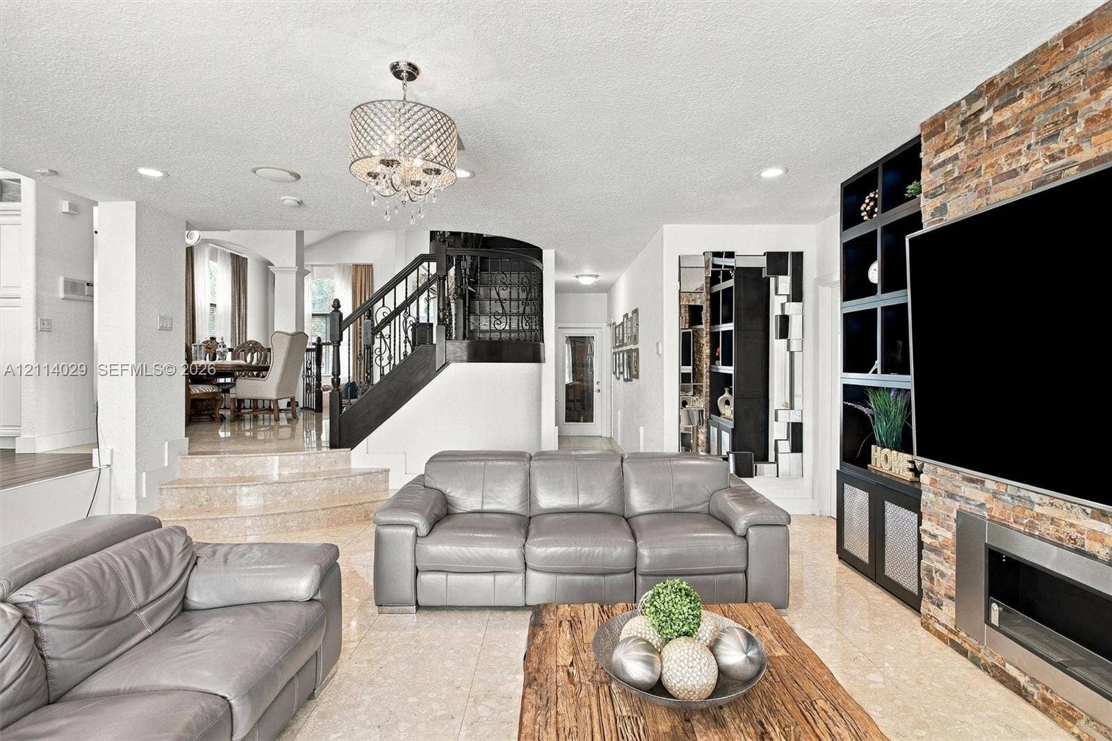 5257 SW 158th Avenue, Miramar, FL 33027 Living area featuring tile flooring, a floor-to-ceiling stone-clad fireplace with built-in dark cabinetry, a multi-tiered staircase with wrought iron railing, and a decorative chandelier