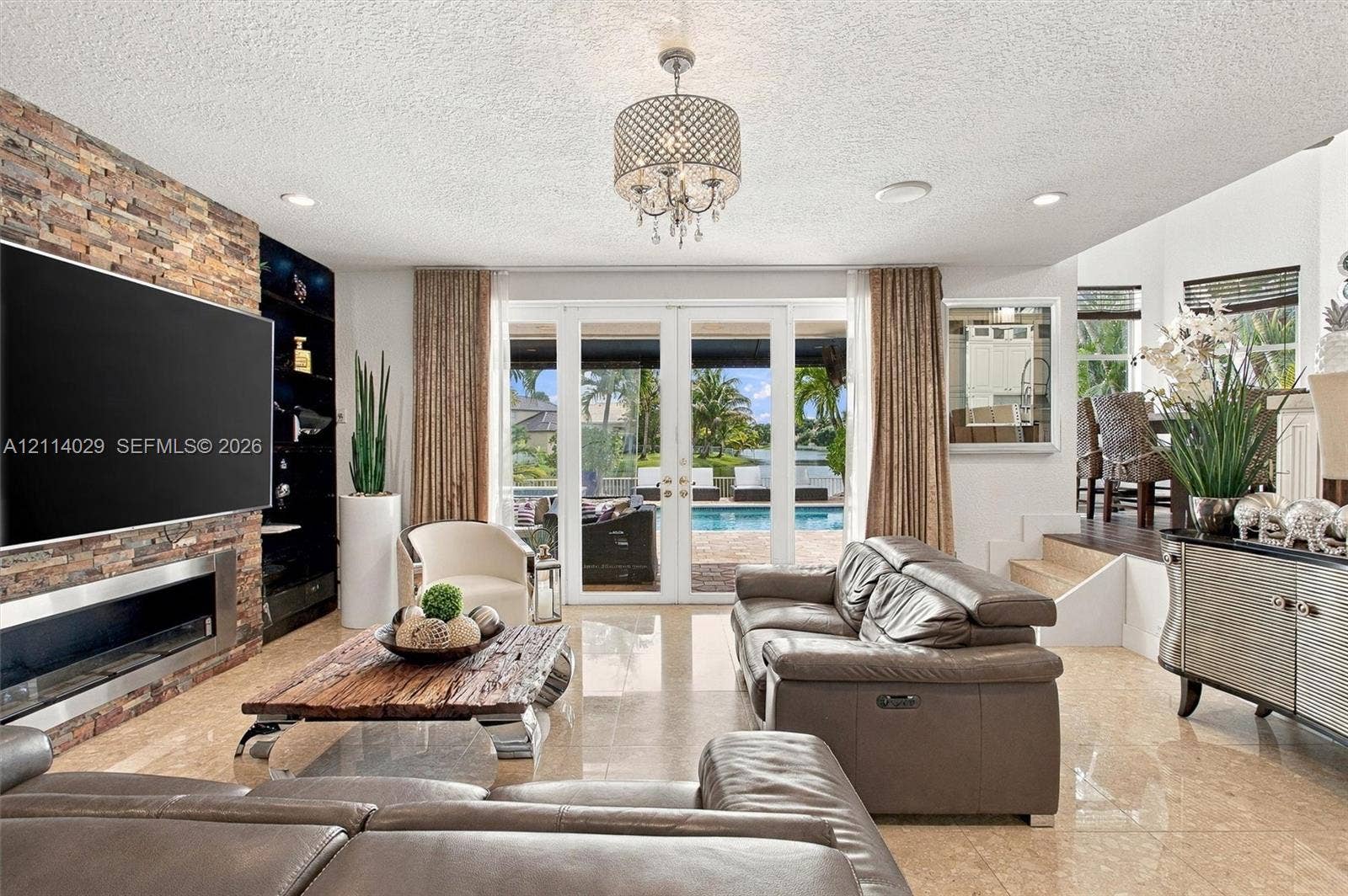 5257 SW 158th Avenue, Miramar, FL 33027 Stacked stone accent wall with integrated linear fireplace, polished stone flooring, and multi-panel glass doors opening to a pool area