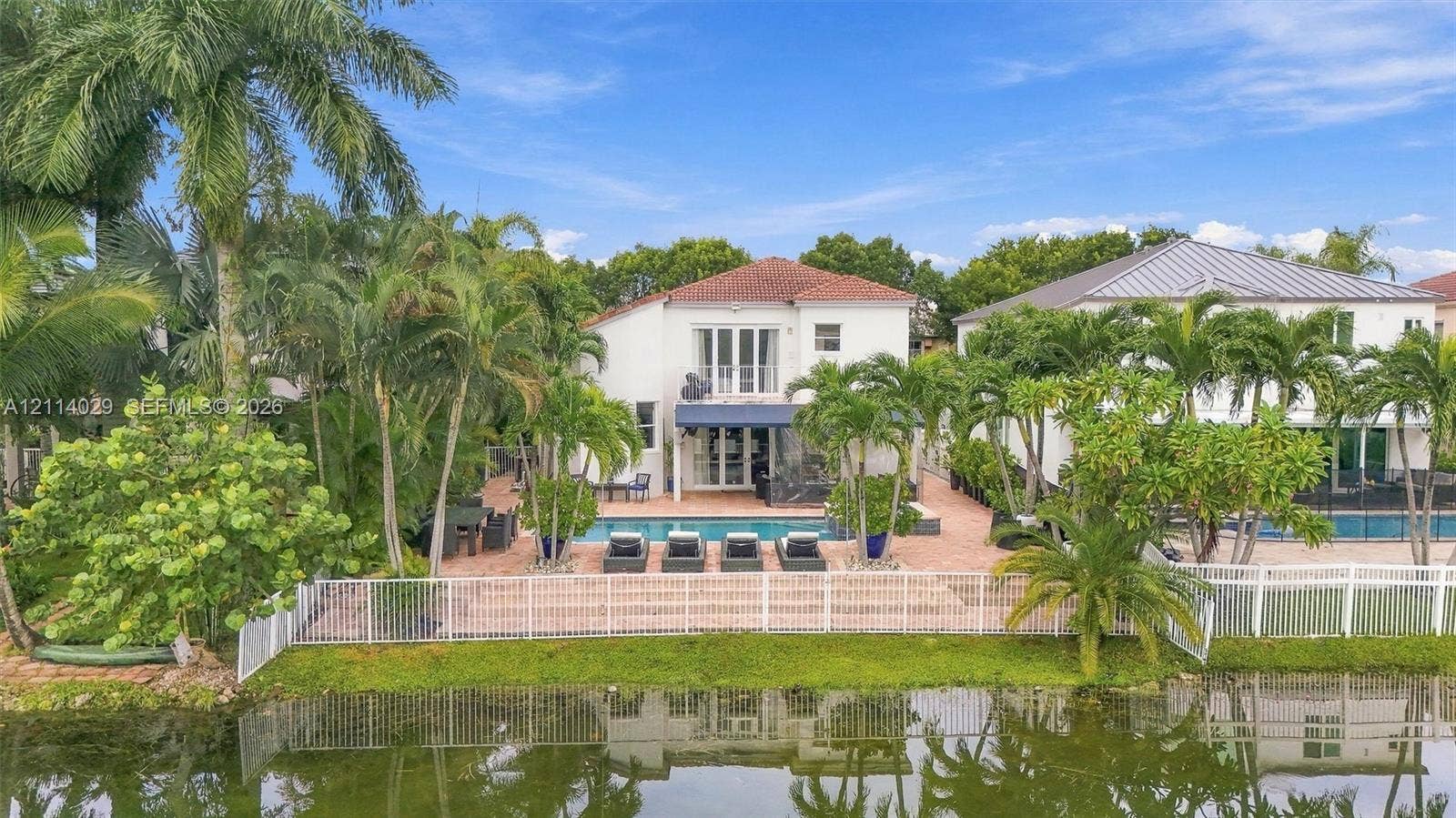 5257 SW 158th Avenue, Miramar, FL 33027 Waterfront residence featuring a swimming pool, paved patio, balcony with glass railing, and mature palm landscaping