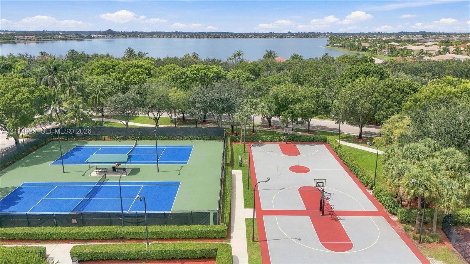 5257 SW 158th Avenue, Miramar, FL 33027 Community recreational area featuring two fenced tennis courts and a basketball court, surrounded by mature trees and proximity to a lake