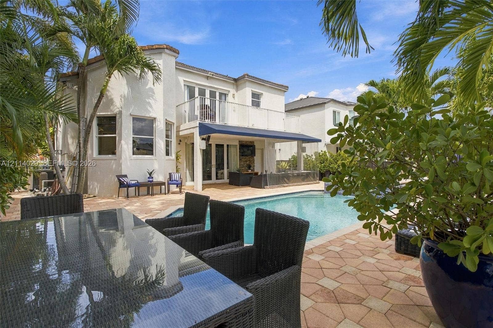 5257 SW 158th Avenue, Miramar, FL 33027 Stucco exterior featuring a second-story balcony with metal railings, a paved stone patio, an in-ground swimming pool, and a retractable awning