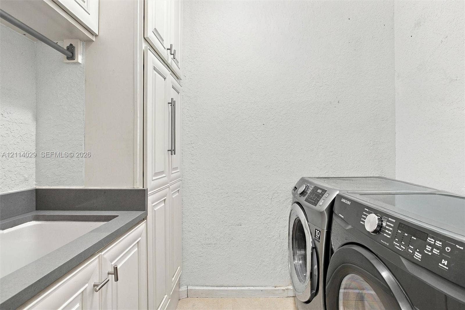 5257 SW 158th Avenue, Miramar, FL 33027 Laundry area featuring full-height white cabinetry, solid-surface countertop, integrated basin, and brushed nickel hardware