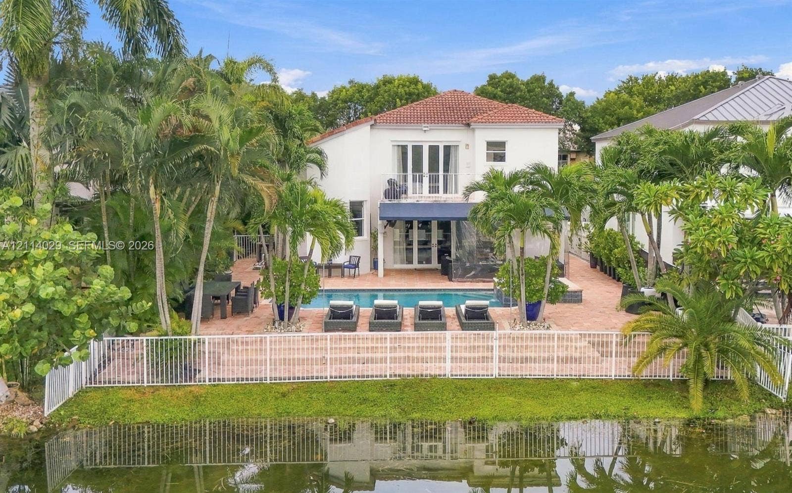 5257 SW 158th Avenue, Miramar, FL 33027 Waterfront rear exterior featuring a swimming pool, expansive brick-paver patio, second-story balcony, and mature tropical landscaping