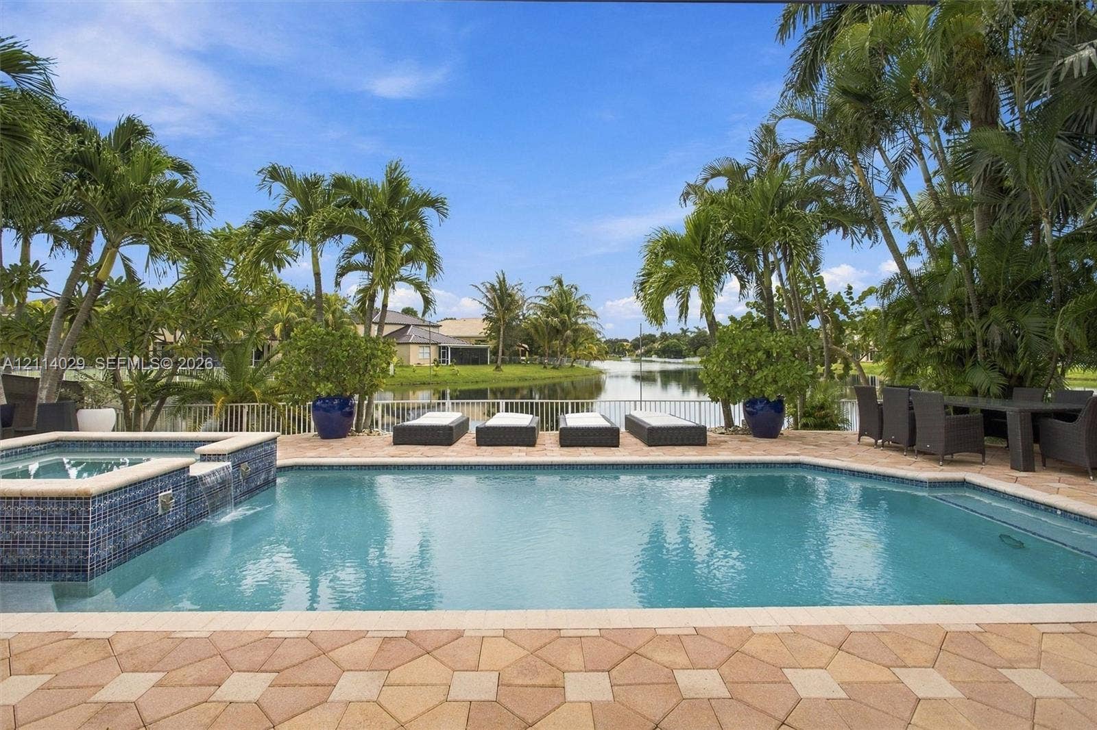 5257 SW 158th Avenue, Miramar, FL 33027 Outdoor pool area featuring a spillover spa with blue glass tile accents, stone paver decking, and waterfront positioning